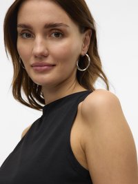 Femeie cu păr castaniu până la umeri, purtând cercei argintii tip cerc și un top negru fără mâneci, uitându-se ușor în lateral cu o expresie neutră.