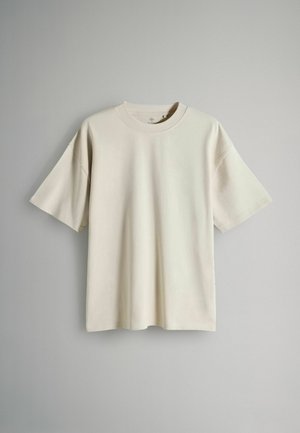 Jasno beżowa krótki rękaw t-shirt wykonana z miękkiego materiału. Posiada okrągły dekolt i luźny krój z opadającymi ramionami. Brak widocznych wzorów lub akcentów.