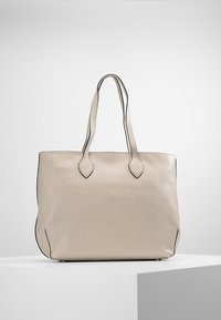Sac fourre-tout en cuir beige avec bordure noire, double poignée et texture lisse. Présente une forme rectangulaire et un design minimaliste.