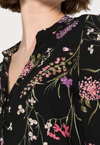Abito nero a fiori con scollatura a V, caratterizzato da colorati fiori ricamati in rosa, viola e verde; tessuto morbido con una finitura leggermente testurizzata.