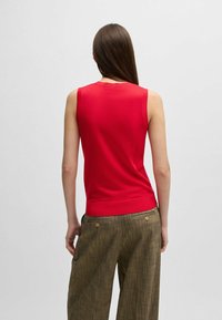 Top rosso senza maniche con un design aderente, texture liscia e orlo a coste, abbinato a pantaloni larghi marroni con texture e gamba larga.