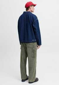 Denimjakke i mørk blå med en avslappet passform, kombinert med olivengrønne kordfløyelsbukser med sidelommer og en teksturert overflate.