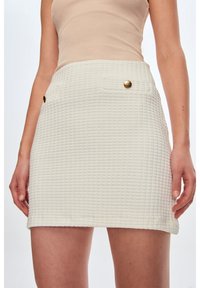 Witte textuur minirok met ruitpatroon, met twee voorzakken en details in goudkleurige knopen.