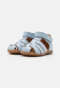 Light blue leather sandals with open toes, featuring three front straps, adjustable Velcro closures, and a flexible brown rubber sole.