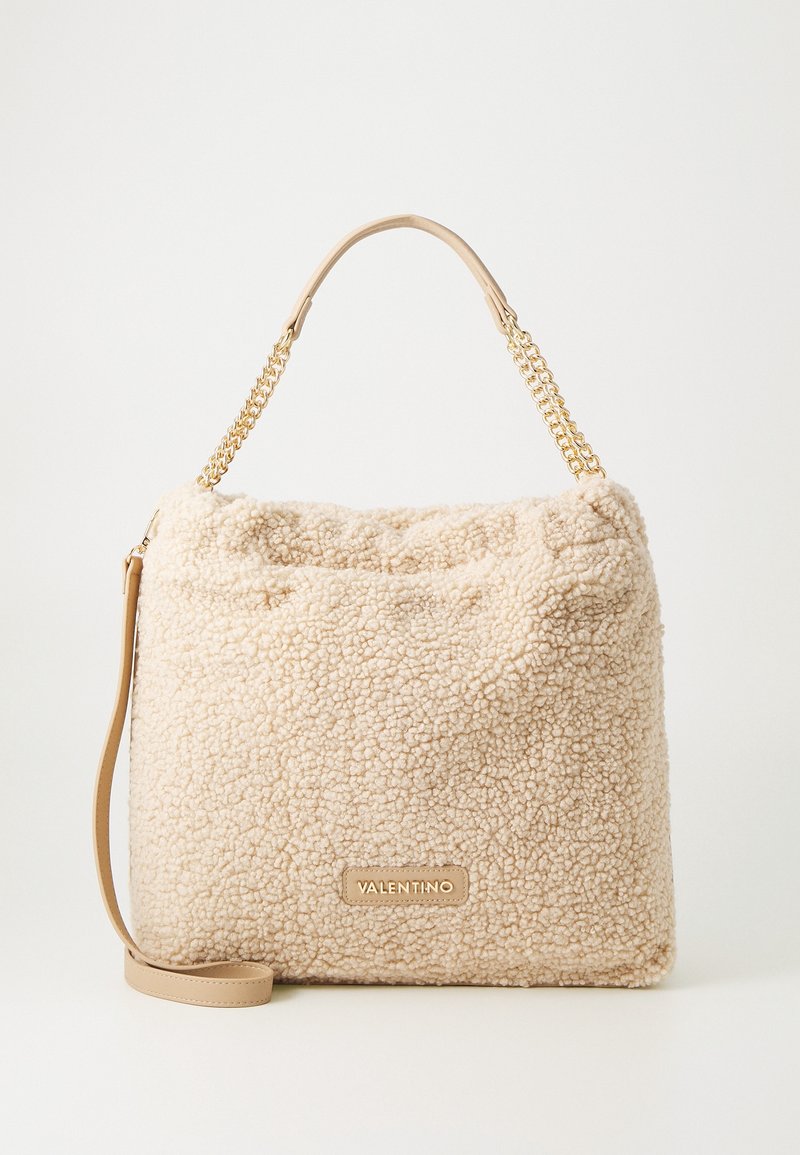 Sac cabas beige en sherpa avec chaîne dorée et poignée en cuir, forme rectangulaire, écusson logo Valentino sur le devant, fond blanc uni.