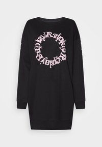 Schwarzer Oversized-Pullover mit langen Ärmeln, ausgestattet mit einem rosa kreisförmigen Logotext in der Mitte und zusätzlichem Text entlang eines Ärmels.