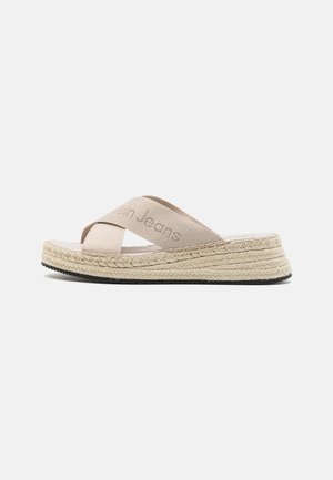 Sandalias de esparto beige con diseño de tiras cruzadas, hechas de tela, con suela de yute y suela exterior de goma negra texturizada.