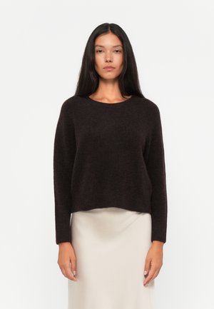 Dark brown sweater with a round neck, long sleeves, and a slightly cropped fit, made of soft, textured fabric. Worn over a light-colored skirt.