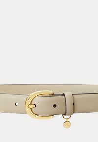 Beige texturerat läderbälte med ett polerat guldspänne i böjd form och en liten rund guldsmycke ingraverad med "RL" som hänger nära öglan.