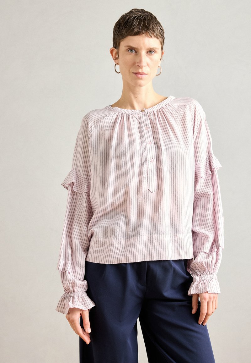 Φωτεινό ροζ μπλούζα με ριγωτή υφή, διαθέτοντας στρογγυλή λαιμόκοψη, κουμπιά και φουσκωτά μανίκια. Συνδυασμένη με ναυτικό χαλαρό παντελόνι.