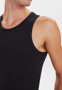 Schwarzes Baumwoll-Top mit Rundhalsausschnitt und weiten Armausschnitten, das eine figurbetonte Passform und eine weiche Textur aufweist.