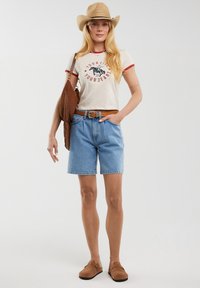 Heledad denim šorts, beež särk punaste aktsentidega, pruun vöö, pruun nubukjalats ja õlgedest cowboy-müts.