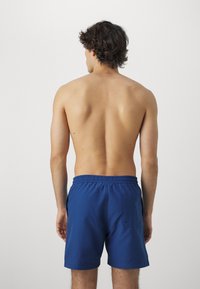 Bañador azul hecho de una tela ligera con cinturilla elástica, bolsillos laterales y un bolsillo trasero. Textura suave con un color sólido.