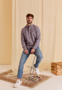 Korte mouwen, knoopshirts met een palmbomenpatroon in roze en blauw, gecombineerd met lichtblauwe jeans en witte sneakers.