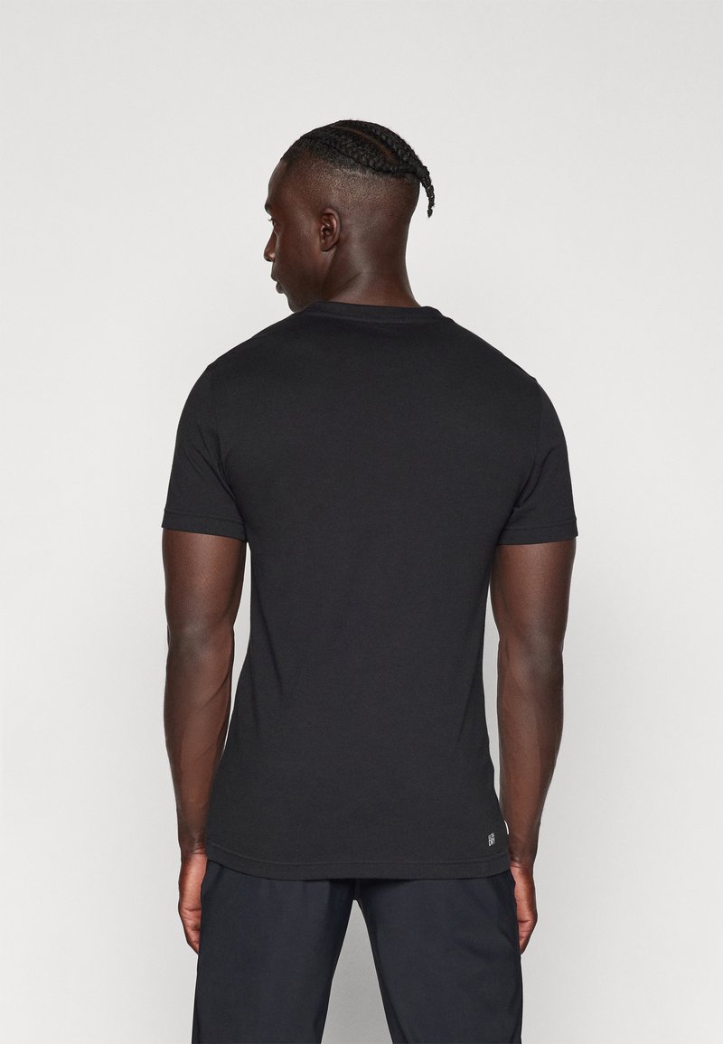 Camiseta negra de manga corta hecha de algodón, con un cuello redondo clásico y un diseño ajustado, con costuras visibles en el dobladillo.