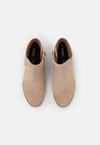 Bottines beiges en daim avec une finition lisse, présentant un design à enfiler, un détail de couture centrale et une fermeture éclair latérale avec des accessoires en or.