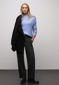 Jasnoniebieski prążkowany sweter z wysokim kołnierzem, zestawiony z ciemnymi, szerokimi spodniami oraz czarnym płaszczem zarzuconym na jedno ramię. Czarne botki do kostek.
