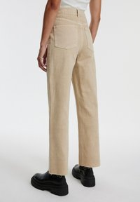 Beige högmidjade jeans med rak benstruktur, som har bakfickor och fransade fållar, kombinerat med kraftiga svarta platåstövlar.