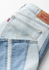 Světle modré džíny z denimu s koženým štítkem, žlutým prošíváním a výraznými zadními kapsami s křivkovými švy a klasickým střihem.