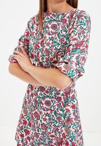 Blumenkleid in Weiß mit pinken und grünen Farbtönen, halblangen Ärmeln und rundem Ausschnitt. Glatte Stofftextur.