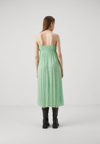 Vestido maxi floral verde con tirantes finos, corsé fruncido y una falda fluida, que presenta pequeñas flores blancas sobre un fondo menta.