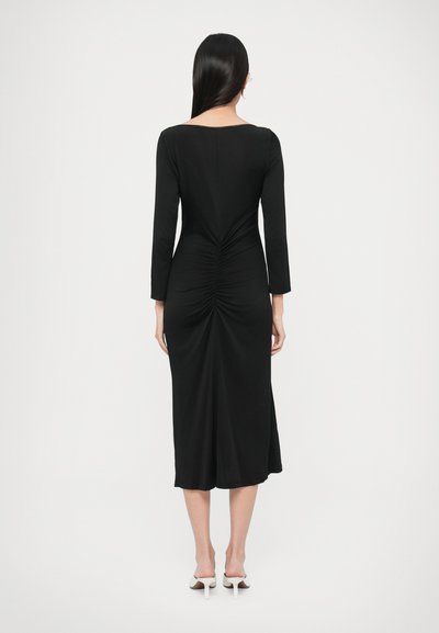 Czarna sukienka z długim rękawem, o kwadratowym dekolcie i marszczeniami z tyłu, sięgająca do połowy łydki. Gładka tekstura.