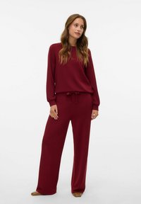 Set da loungewear bordeaux composto da una maglia a maniche lunghe e pantaloni a gamba larga con un cordoncino regolabile. Tessuto morbido e vestibilità comoda.