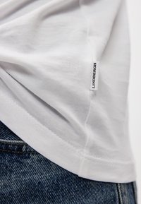 Hvit bomulls T-skjorte med en myk, glatt tekstur. Har et lite svart "Lindbergh" merke på siden og rett kant, kombinert med denim.