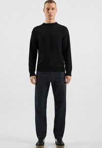 Pull en tricot noir, col rond, manches longues ; associé à un jean droit foncé et des baskets noires avec une semelle texturée.