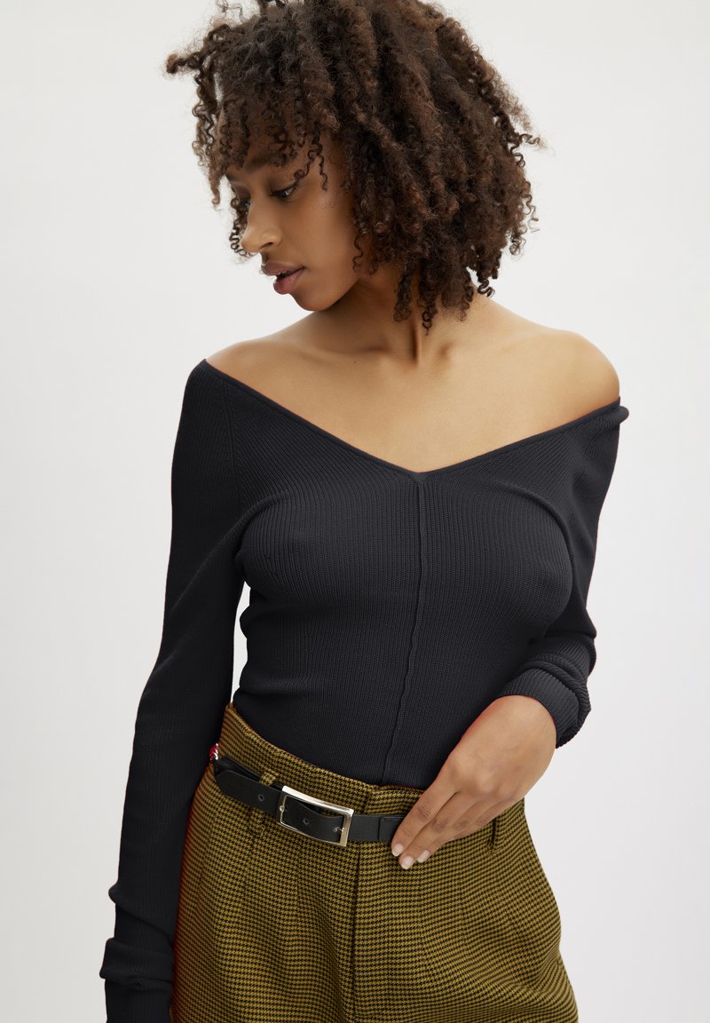 Top negru cu dungi, cu mânecă lungă și guler de tip off-shoulder, combinat cu o pereche de pantaloni tratați galbeni cu motiv houndstooth, având talie înaltă și o curea neagră.