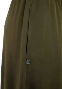 Gonna verde oliva con una texture morbida, dotata di una tasca laterale e di un piccolo logo metallico vicino all'orlo.