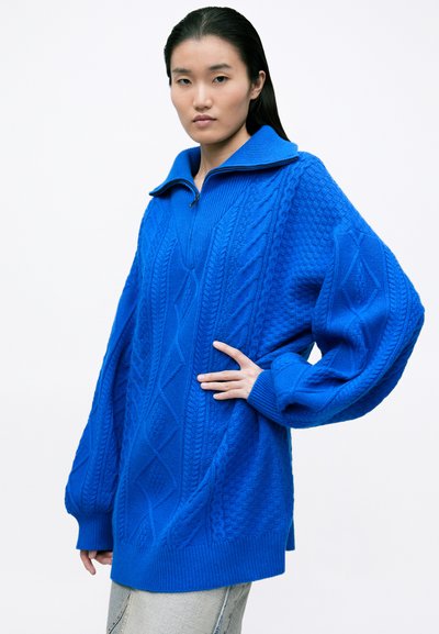 Su�éter de punto azul brillante con un cuello alto y media cremallera, que presenta patrones de punto trenzado texturizado y mangas de gran tamaño.