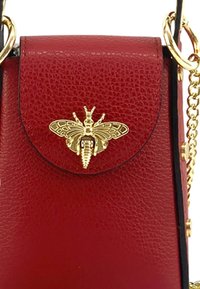 Rode leren handtas met textuur, gouden bijembleem op de klep en een gouden kettingriem om te dragen.
