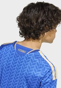 Blå sporttröja med bladmönster, guldfärgade detaljer och en nätkrage med texten "AZZURRA" på baksidan av halsen.