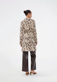 Μπεζ παλτό με animal print, με εφαρμοστό μέσο, μακριά μανίκια και απαλό υφή, σε συνδυασμό με σκούρα γυαλιστερά παντελόνια και καφέ ψηλοτάκουνα.