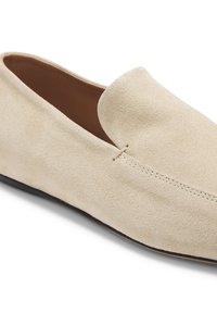 Mocassin beige en daim avec un bout arrondi, un design sans lacets et des coutures visibles le long du bord supérieur et du dessus.