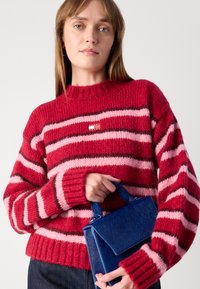 Rood- en roze gestreepte gebreide trui met geribbelde manchetten en zoom, gecombineerd met een blauwe gestructureerde handtas met een textuurafwerking.