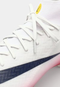 White athletic shoe featuring a textured upper, navy blue design accent, flat white laces, and a pink gradient sole with branding detail.