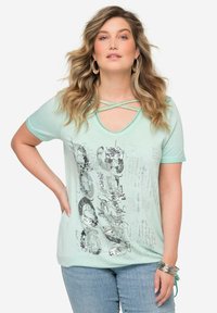 Camiseta de color verde menta de manga corta con cuello en V y tiras cruzadas, adornada con texto en lentejuelas plateadas y un estampado gráfico.