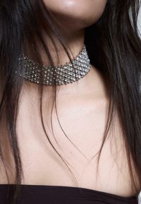 Strass-Choker mit mehreren Lagen, in Silberfarbe, mit rautenförmigen Mustern und einer strukturierten Oberfläche, am Hals getragen.