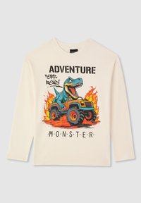 Kremowa koszulka z długim rękawem z motywem dinozaura prowadzącego monster trucka, z ogniem i wyraźnym tekstem: "PRZYGODA POZA DROGAMI MONSTER."