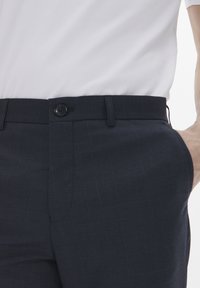 Pantalones de cuadros marinos con una textura suave, que cuentan con cierre de botón, trabillas para cinturón y bolsillos laterales. El diseño incluye patrones de cuadros sutiles.