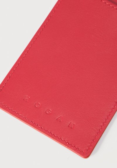 Φωτεινό κόκκινο δερμάτινο ορθογώνιο θήκη καρτών με ραμμένα άκρα, με ανάγλυφο το όνομα της μάρκας "HOGAN" κοντά στο κάτω μέρος.