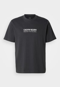 Melnā kokvilnas īsroku T-krekls ar apaļu kakla izgriezumu un baltu "CALVIN KLEIN NEW YORK EST. 1968" logotipu priekšpusē.