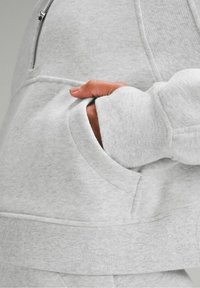 Sweat à capuche gris avec poche avant, poignets côtelés et texture lisse et douce. Col ajustable avec fermeture éclair et coutures surpiquées.