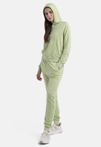 Sudadera y pantalones jogger verde claro hechos de una tela suave. La sudadera cuenta con un bolsillo frontal y puños acanalados. Combinados con zapatillas deportivas blancas.