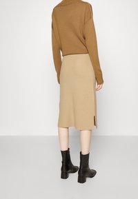 Brun stickad tröja med ribbad halsringning och ärmar, matchad med en beige ribbad midikjol med en sidoklyvning, bärs med svarta ankelskor.