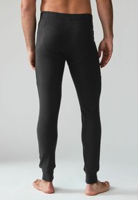 Pantalons thermiques noirs, ajustés, avec une texture côtelée. Poignets aux chevilles et ceinture lisse. Conçus pour la chaleur et le confort.