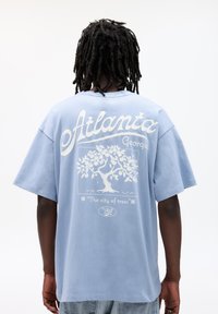 Light blue oversized t-shirt featuring white text "Atlanta Georgia," an outline of a tree, and the phrase "The city of trees."