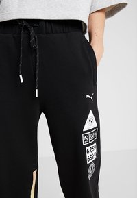 Zwarte sweatpants in een katoenmengsel met een trekkoord in de taille, voorzien van witte grafische prints en een kleurgeblokkeerde accent aan de zijkant.